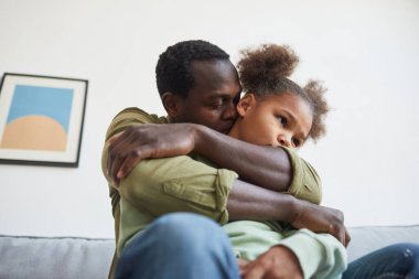 Afro-Amerikalı babayı sevmenin düşük açılı portresi. Sevimli kızı kucaklar. Ev içi, kopya alanı.