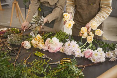 Background image of beautiful flowers on table in flower shop with two unrecognizable florists arranging bouquets, copy space