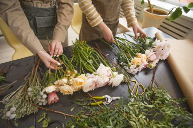 Close up of beautiful flowers on table in flower shop with two florists arranging bouquets, copy space