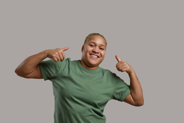 Талия вверх портрет андрогинной смешанной расы женщина улыбается в камеру, позируя на сером фоне в студии и показывая большие пальцы вверх, скопировать пространство
