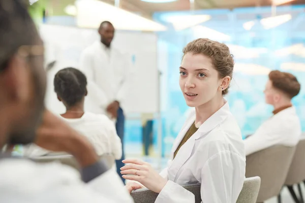 医学セミナー中に男と話をしながら研究室のコートを着た若い女性の肖像画 コピースペース — ストック写真