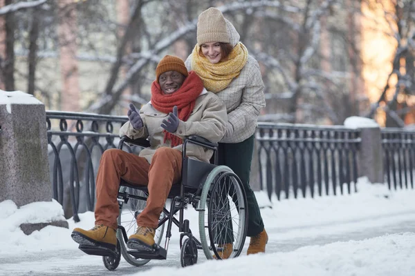 アフリカ系アメリカ人男性の車椅子を使用して 冬には屋外で楽しい笑顔の若い女性を支援し スペースをコピーします — ストック写真