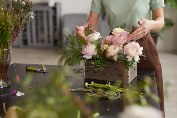 Cropped portrait of unrecognizable young woman arranging flower composition with pink peonies while working in florists workshop, copy space