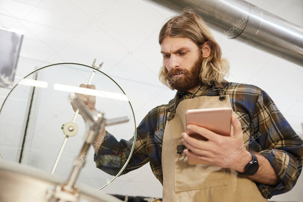 Low angle portrait of bearded brewmaster inspecting production at beer making factory, copy space