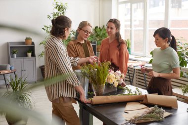 Wide angle view at diverse group of young florists arranging floral compositions while working in flower shop