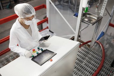 Modern kimya fabrikasında çalışan kadın işçilerin yüksek açılı portresi kontrol panelinde düğmelere basarken aynı zamanda makine birimlerini çalıştırıyor, boşluğu kopyalıyor