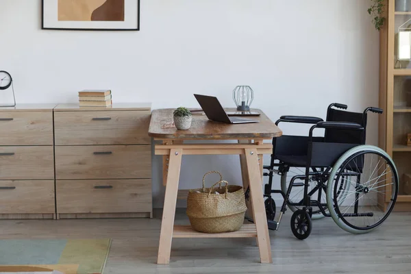 Background image of empty wheelchair by desk at accessible home office workplace, copy space