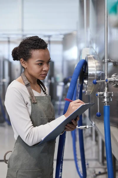産業食品工場で生産品質を検査しながらクリップボードを保持している若いアフリカ系アメリカ人女性の垂直肖像画 コピースペース — ストック写真