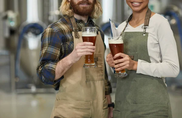 ビールグラスを手にした2人の笑顔の若い労働者の群像と醸造工場でのワークショップに立っている間のカメラを見て スペースをコピー — ストック写真