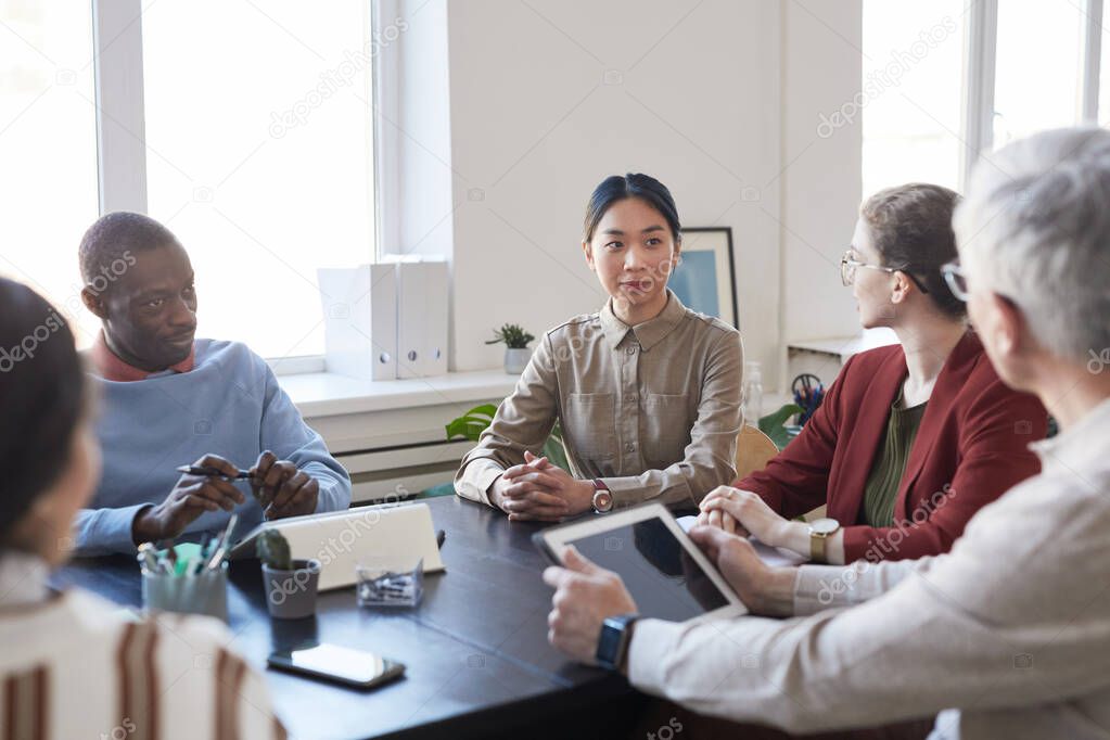 Diverse group of business people during briefing meeting in office, focus on young Asian businesswoman listening to boss