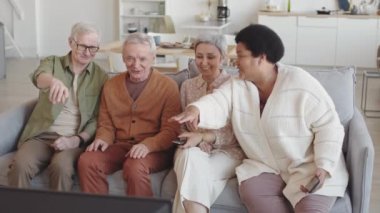 Orta uzunlukta, dört farklı etnik çeşitlilikte üst düzey insanın oturma odasında birlikte oturup TV 'de komik programlar izlemesi, konuşması ve gülmesi.