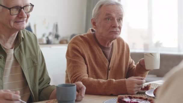 家のテーブルに座っている2人の上級白人男性の傾き 甘いケーキを食べ お茶を飲み 認識できない人々と話す — ストック動画