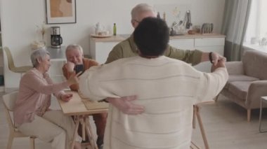 Üst düzey Kafkasyalı kocasıyla dans eden mutlu Afrikalı kadının yüksek açılı görüntüsü. Arkadaşları onları akıllı telefondan yemek masasında otururken filme alıyor.
