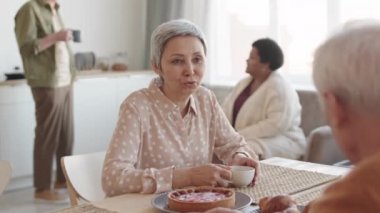 Gülümseyen, masada oturan, çay içen, tanınmayan bir arkadaşla konuşan neşeli, kıdemli Asyalı kadının belinden yukarı doğru.