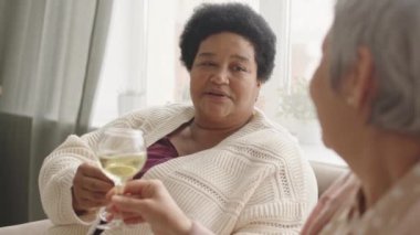 Neşeli, olgun bir Afrikalı kadının evinde kanepeye oturup beyaz şarap içmesi, tanınmayan bir arkadaşla konuşup gülmesi.