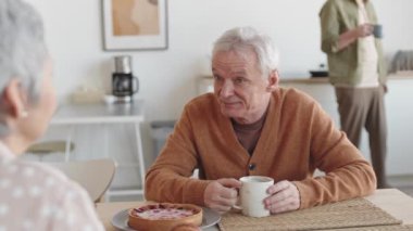 Gülümseyen, masada oturan, çay içen, tanınmayan bir arkadaşla konuşan neşeli, kıdemli, beyaz bir adamın belinden yukarı doğru.