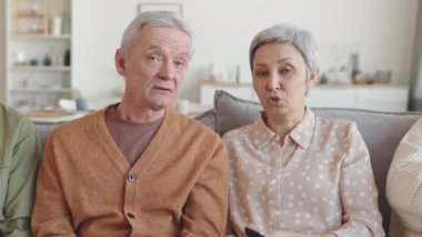 Yaşlı beyaz bir adam ve Asyalı bir kadının belinde oturarak kanepede oturup, görünmez TV seyrederek, tartışarak, gülümseyerek, parmaklarını göstererek.