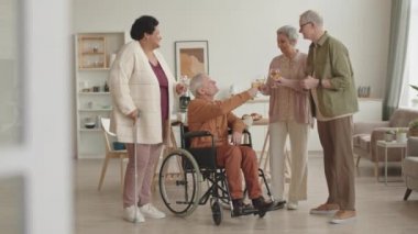 Bastona yaslanmış Afrikalı bir kadın, tekerlekli sandalyedeki engelli bir adam, gri saçlı Asyalı bir kadın ve apartmanda beyaz şarap içen yaşlı beyaz bir adam.