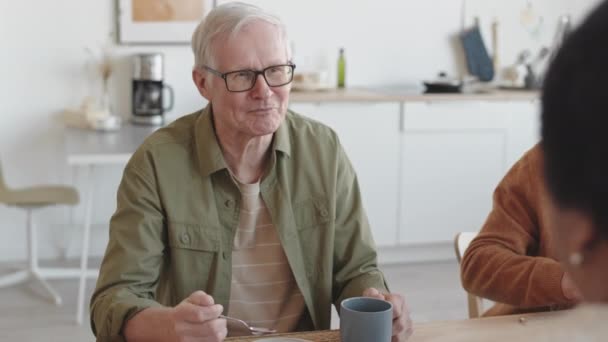 开心的白人老人面带微笑 坐在桌旁 吃着甜蛋糕 和不认识的人交谈 — 图库视频影像