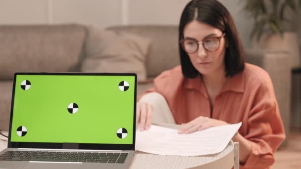 Steadicam Niewyraźne Ciemnowłosa Kobieta Siedzi Salonie Patrząc Przez Papiery Laptop — Wideo stockowe