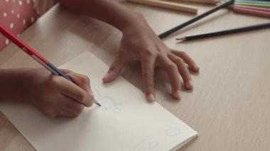Kağıda kalem çizen tanınmayan bir çocuğun yüksek açılı görüntüsü.
