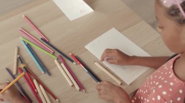 Masaya kalemle kartpostal çizen tanınmayan iki çocuğun yüksek açılı elleri.