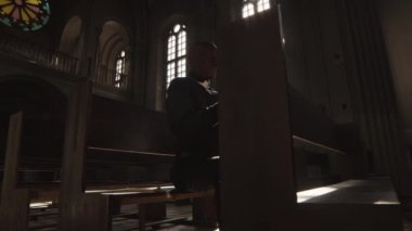 Siyah elbiseli, beyaz yakalı Afro-Amerikan bir papazın solunda oturuyor Katolik kilisesinde oturuyor ve İncil okuyor.