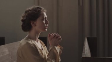 Hıristiyan kilisesindeki ahşap sıralarda oturan beyaz bir kadının elleri bağlı dua eden ve Tanrı 'ya dua eden bir portresi.
