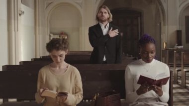 Lüteriyen kilisesinde sıralarda oturup İncil okuyan iki genç kadını kilit altında tutarken, beyaz bir adam arka planda dua edip haç çıkarıyordu.