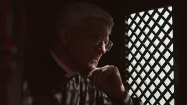 Kafkasyalı yaşlı rahiplerin kaftan, beyaz yakalı ve gözlüklü günah çıkarma odasında ellerinde İncil 'le oturup ahşap pencereden cemaat üyeleriyle sohbet etmeleri.