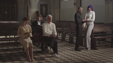 Lüteriyen kilisesindeki sıralarda oturan üç beyaz kilise üyesinin Afrikalı-Amerikalı papazın yakınlardaki genç Afrikalı bir kadınla konuşurken geniş açılı görüntüsü.