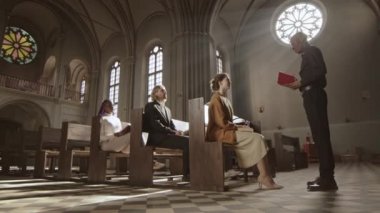 Lüteriyen kilisesinde elinde İncil 'le siyah pantolon, gömlek ve beyaz yakalı bir papazın kilise cemaatinden biriyle konuşurken geniş açılı görüntüsü.