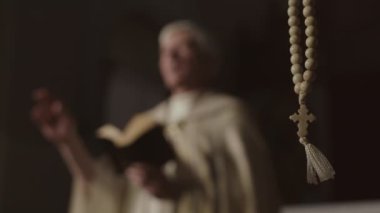 Hıristiyan kilisesinde asılı tespih boncukları ve arka planda vaaz veren bayramlık altın bornoz giyen tanınmayan yaşlı rahipler.