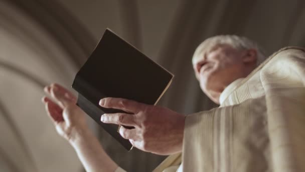 白人老年牧师穿着节日金色长袍站在基督教教堂 手里拿着 在婚礼上布道的低视角图像 — 图库视频影像
