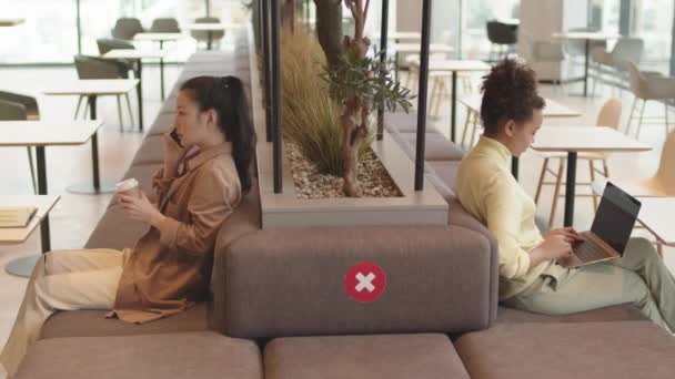 亚洲女性顾客通过电话交谈 喝咖啡 使用笔记本电脑 坐在餐厅沙发上 沙发背面有交叉的红色标志等中长的侧面画面 — 图库视频影像