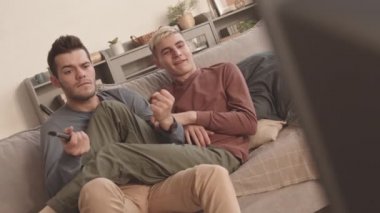 Evdeki kanepede oturan, TV 'de müzik programı izleyen ve mikrofon olarak TV kumandasını kullanan neşeli, neşeli, beyaz bir çifti kilit altında tutuyorlar.