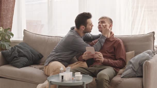 一个年轻的白种人坐在家里的沙发上 用棉垫擦拭男朋友的脸 — 图库视频影像
