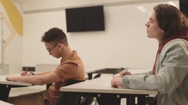 在大学课堂上 白人年轻男生在考试中与同学作弊 坐在他面前的侧视图 — 图库视频影像