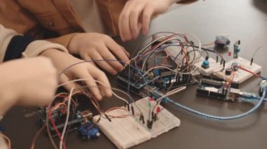 Sınıfta masasında oturan tanınmayan iki öğrencinin yüksek açılı görüntüsü ve birlikte fütürist robotlar yapmaları.