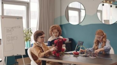 Robot teknolojisi dersi sırasında farklı detaylar ve kablolar kullanarak sınıftaki masasında oturan iki genç beyaz erkek ve kızın kilitlenmesi.