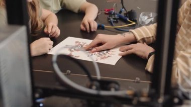 Tanımlanamayan bir kadın ve iki okul öğrencisinin atölyede oturup robotların...