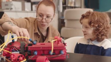 Yuvarlak gözlüklü, kıvırcık saçlı, sınıfın en üst katında oturan ve elektronik robot üreten kızıl saçlı genç kız öğretmenler.