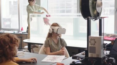 Üç beyaz okul öğrencisinin okul laboratuarında vakit geçirmesi. Çocuk arka planda robo botu suya koyarken, genç kız VR gözlük takıyor.