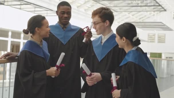 Tilt Four Diverse Students Wearing University Graduate Gowns Standing Indoors — Stock Video