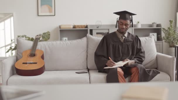 Encierro Joven Estudiante Afroamericano Con Vestido Graduación Sombrero Sentado Sofá — Vídeo de stock