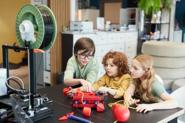 High angle portrait of three children building robot boat together during engineering class at modern school, copy space