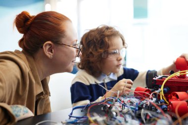 Side view portrait of female teacher helping boy building robot during engineering class at school