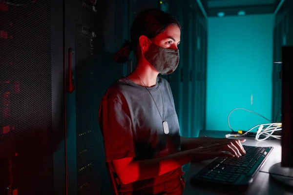 コンピュータを使用している間にマスクを着用し 赤い光に照らされたサーバールームで作業する女性Itエンジニアの肖像画 コピースペース — ストック写真