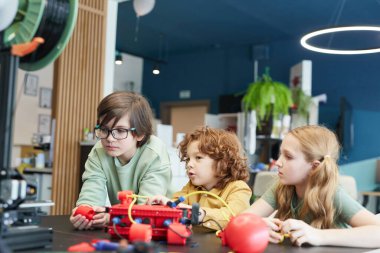 Portrait of three children operating robots during engineering class at modern school, copy space