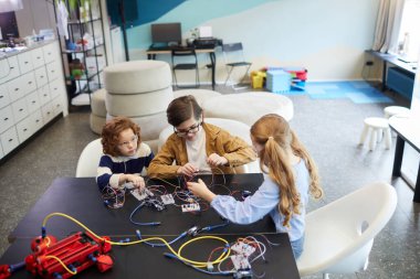 High angle view at group of children building robots and experimenting with electric circuits in engineering class at school, copy space